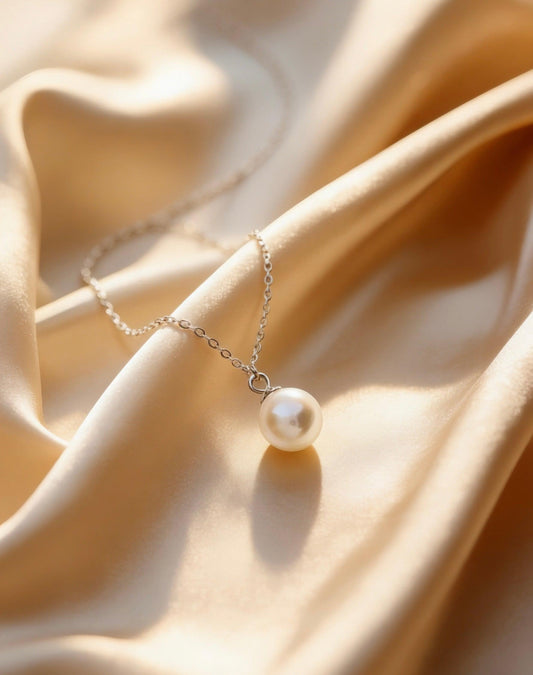 Single pearl drop necklace on soft champagne silk background, luxury women's accessory