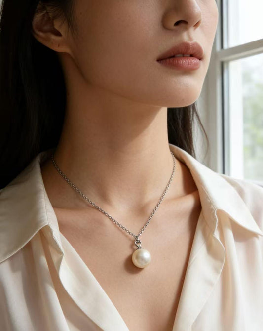 A sterling silver chain with a round white pearl pendant worn by an Asian model on a neck with light skin, styled with an unbuttoned cream shirt."