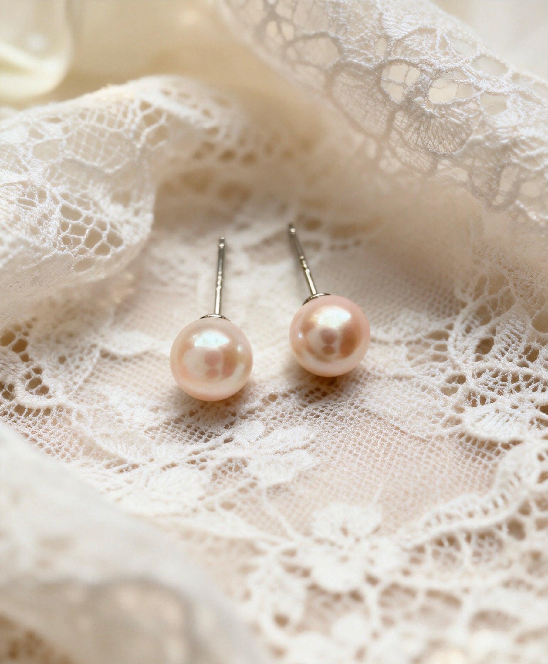 Pair of 7mm natural pink freshwater pearl stud earrings with sterling silver posts on white lace.
