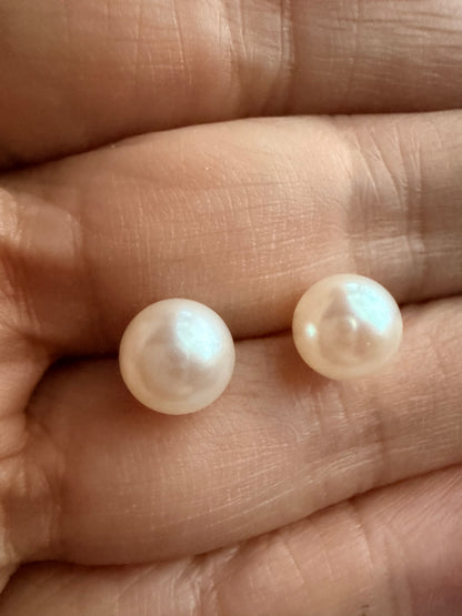 Two luminous 7mm freshwater pearl stud earrings with sterling silver posts, held in a hand.