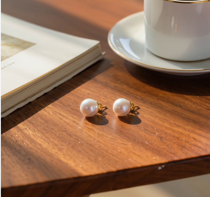 Two 7mm white freshwater pearl stud earrings with gold-toned posts on a wooden table.