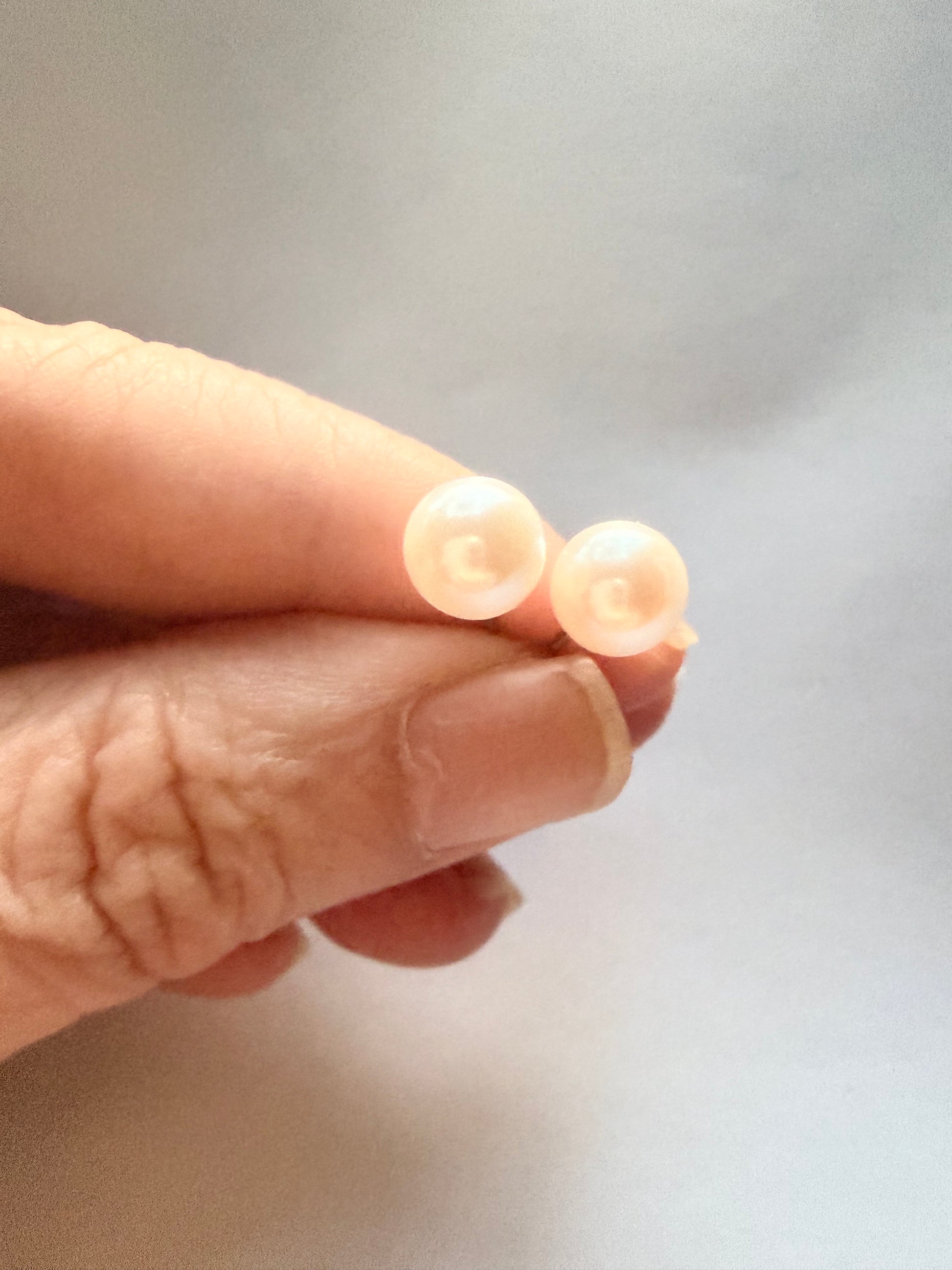 Hand holding two 7mm natural freshwater pearl stud earrings with sterling silver posts.
