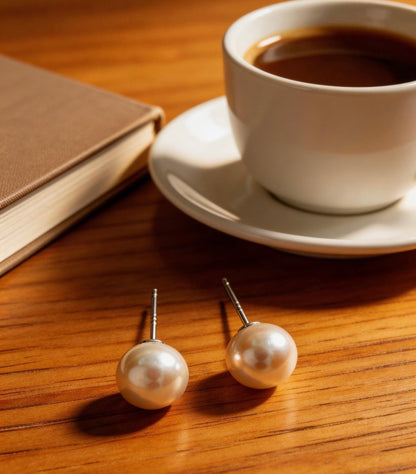 7mm freshwater pearl stud earrings with sterling silver posts on a wooden table next to coffee and a book.
