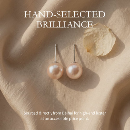 Pair of round, lustrous pink South Sea pearl stud earrings with sterling silver posts on a beige fabric.