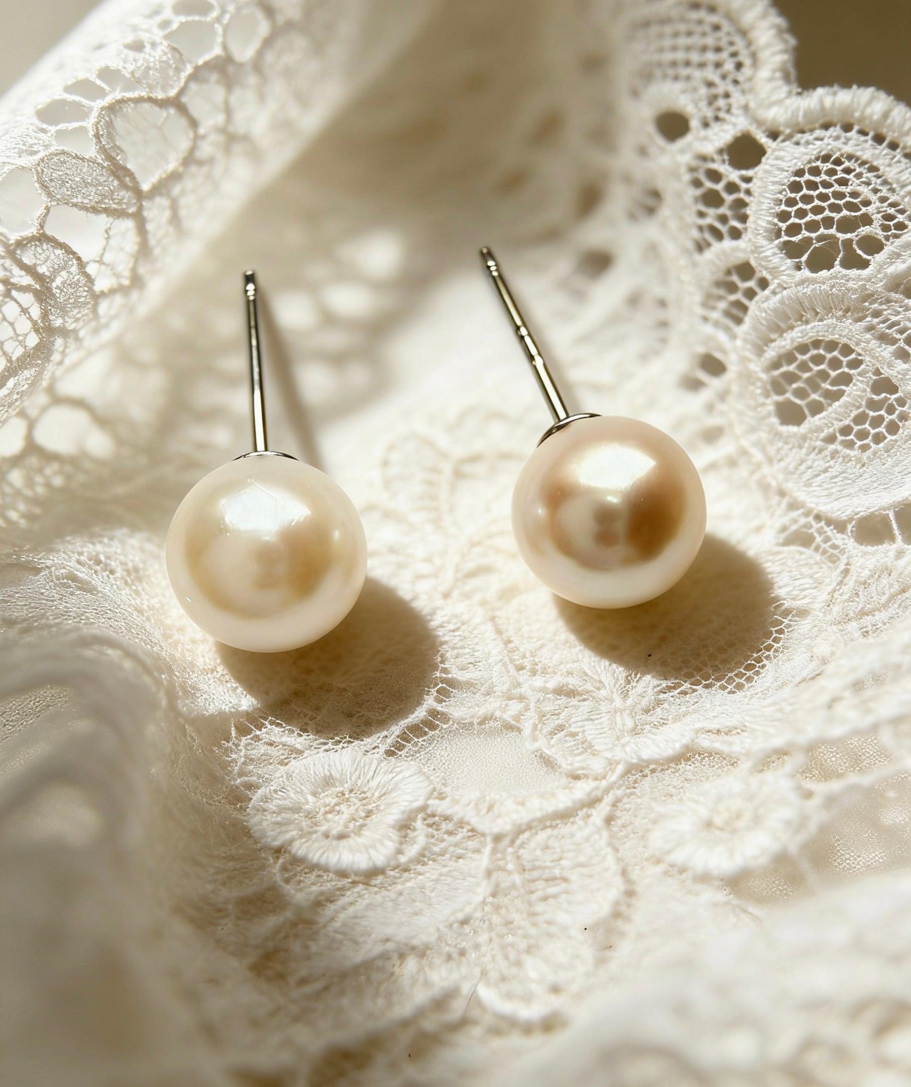 Two 7mm natural saltwater Hepu pearl stud earrings with sterling silver posts on white lace.