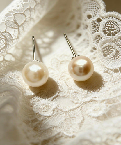 Two 7mm natural saltwater Hepu pearl stud earrings with sterling silver posts on white lace.