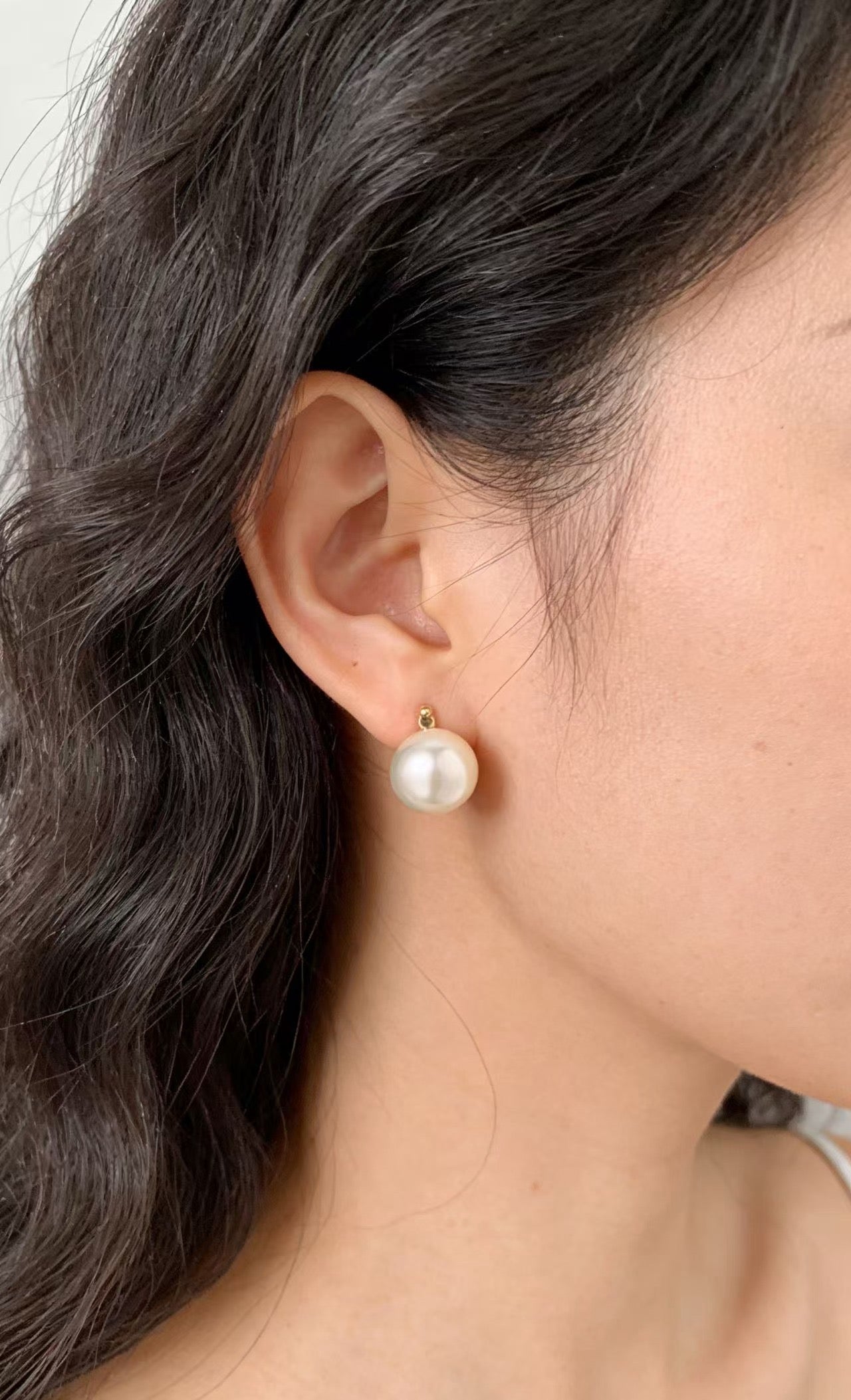Luvymia 7mm South Sea pearl stud earring with gold-tone setting on a woman's ear.