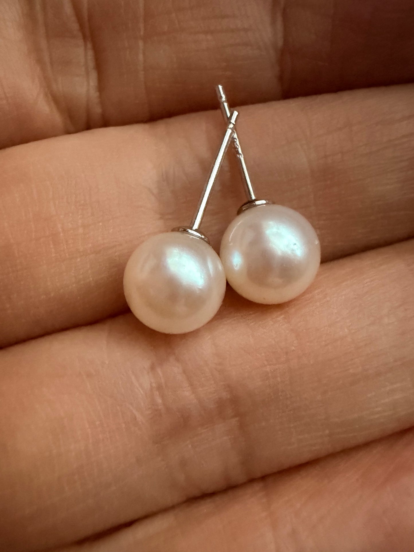 Pair of 6-7mm round South Sea pearl stud earrings with sterling silver posts, held in a hand.