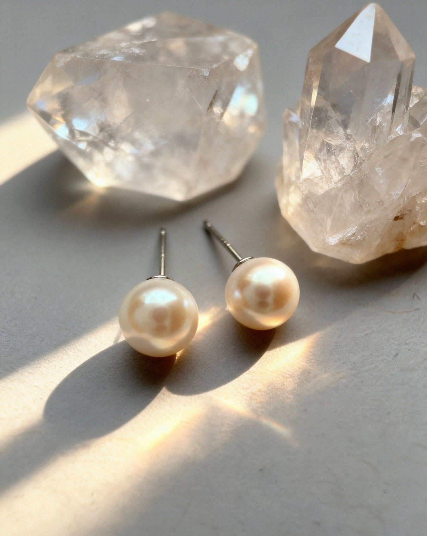 Luvymia 7mm South Sea pearl stud earrings with natural luster and sterling silver posts, beside clear quartz crystals.