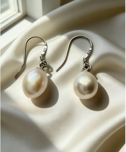 Baroque freshwater pearl drop earrings with 925 sterling silver hooks on a cream satin fabric.