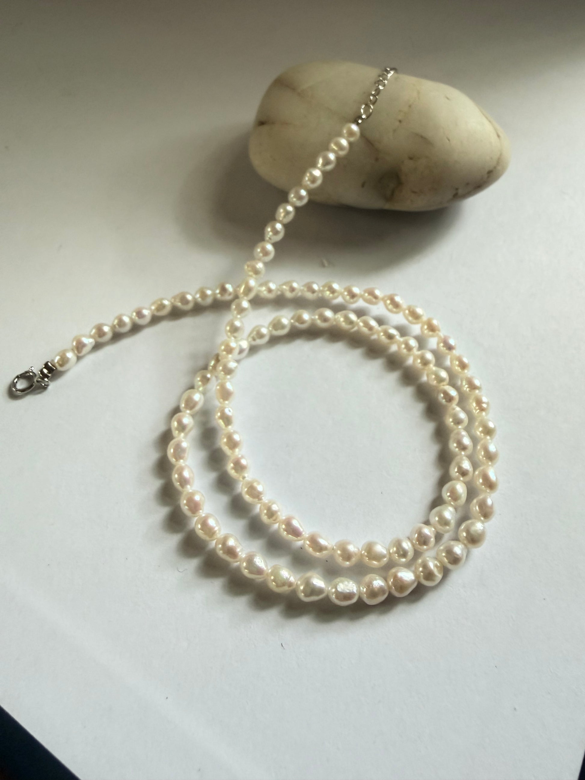 Baroque freshwater pearl necklace with 3-4mm seed pearls and 925 sterling silver clasp, coiled on white.