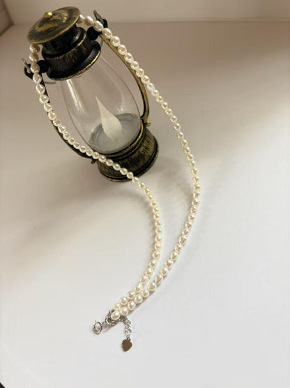 Baroque freshwater pearl necklace (3-4mm) with 925 sterling silver clasp and heart charm, draped over a lantern.