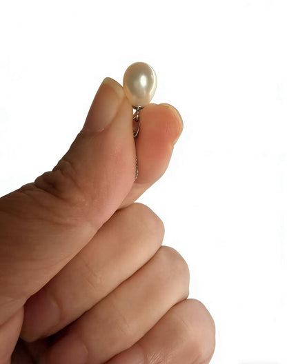Hand holding a single cream-white baroque freshwater pearl pendant with a delicate silver chain.