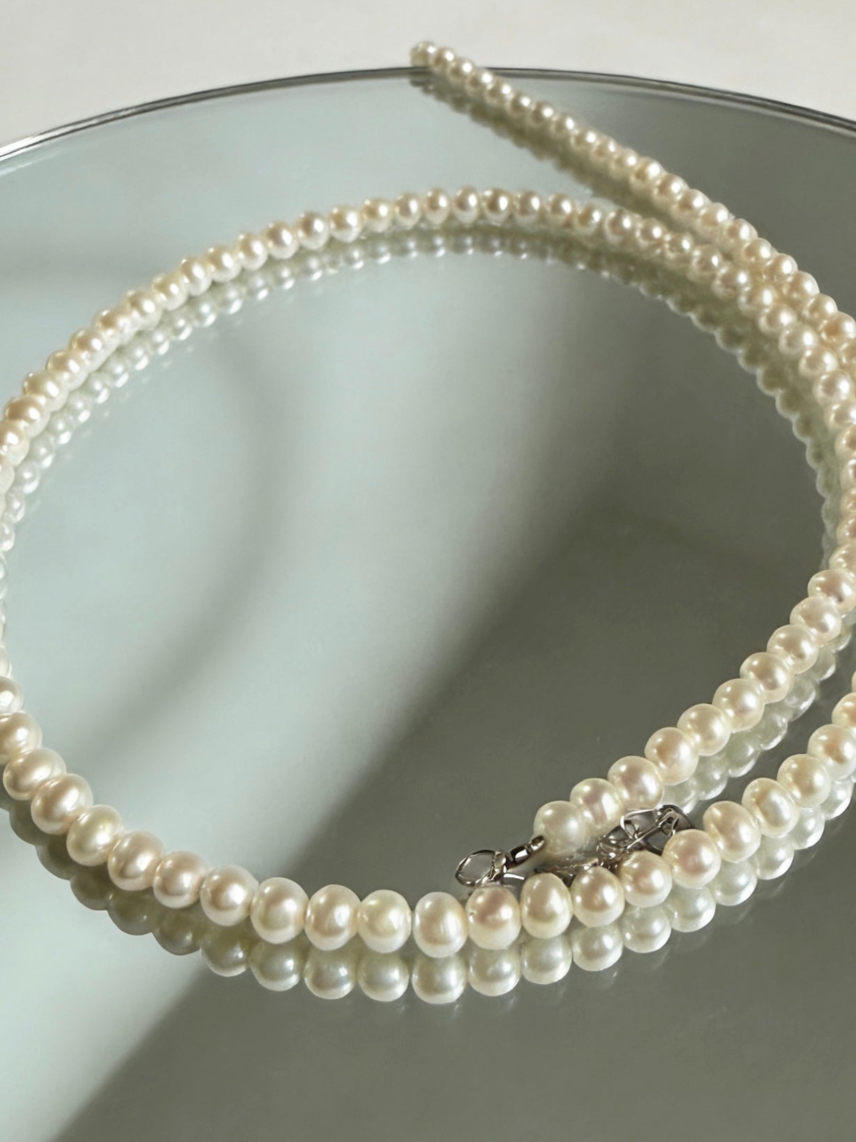 Luvymia 3-4mm near-round freshwater pearl necklace with 925 sterling silver clasp on a mirror.