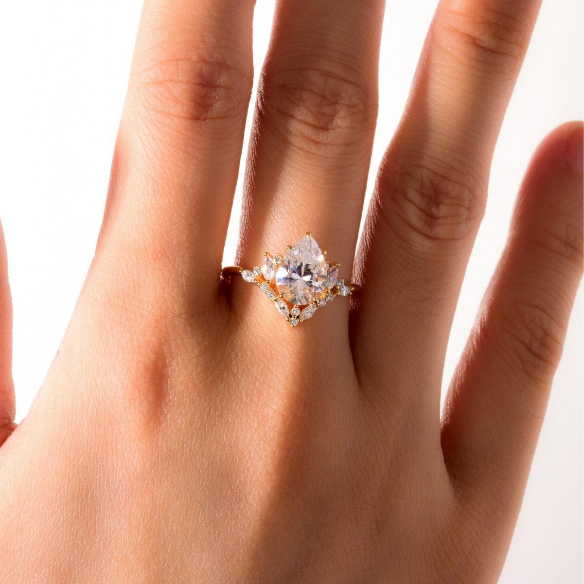 Pear-cut moissanite halo ring with marquise and pavé accents on a gold band.