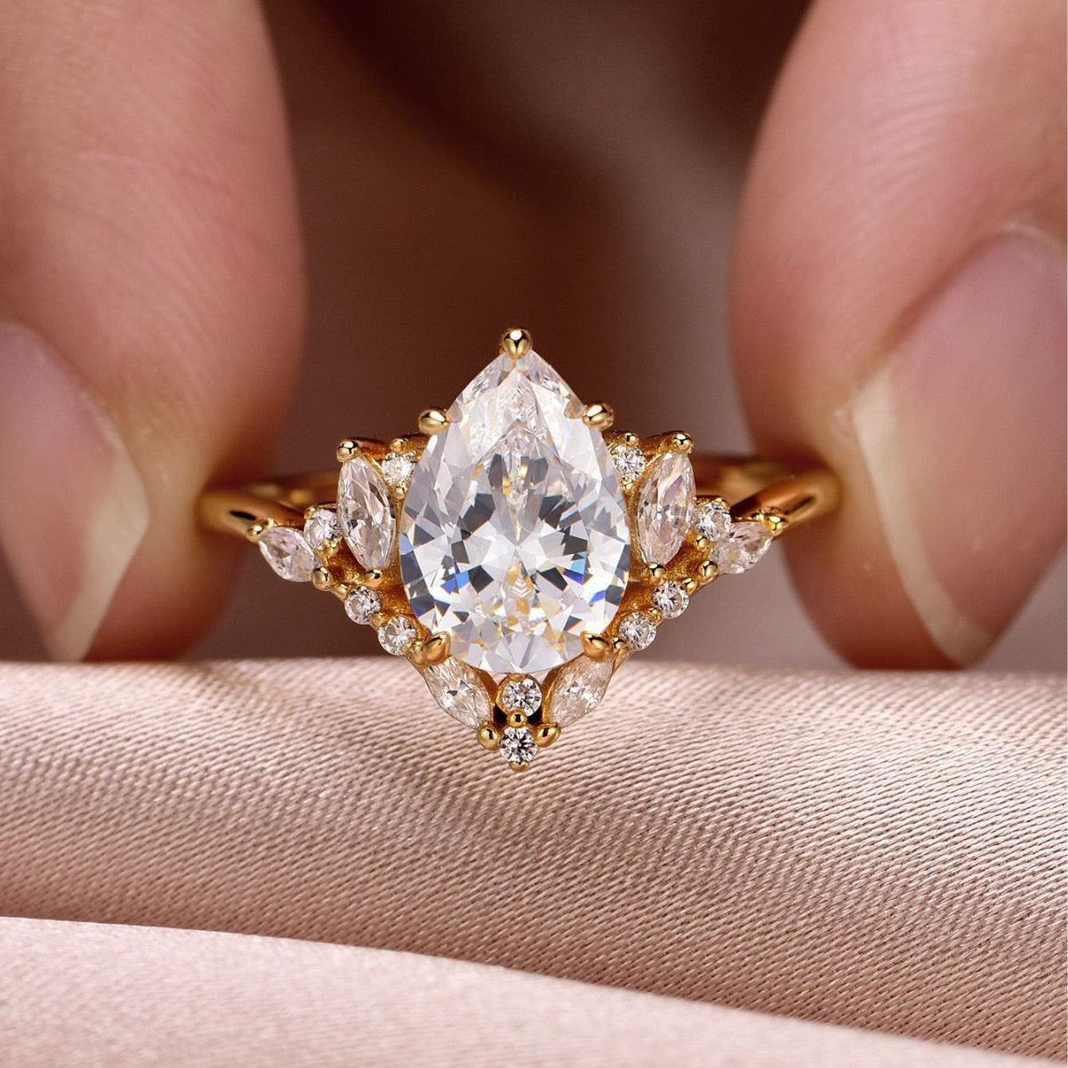 8x12mm pear-cut D color moissanite halo ring with marquise and pavé accents on a gold band.